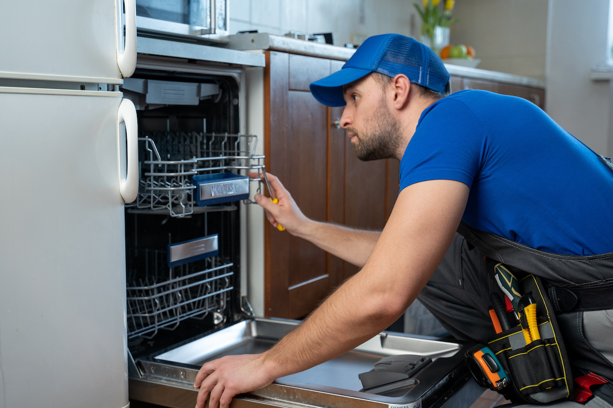 repair of dishwashers. repairman repairing dishwasher in kitchen